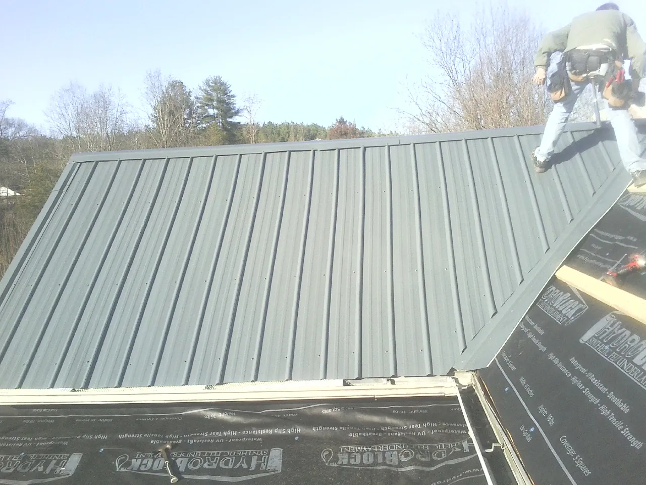 Crew installing dark green standing seam panels over synthetic underlayment in Castalia