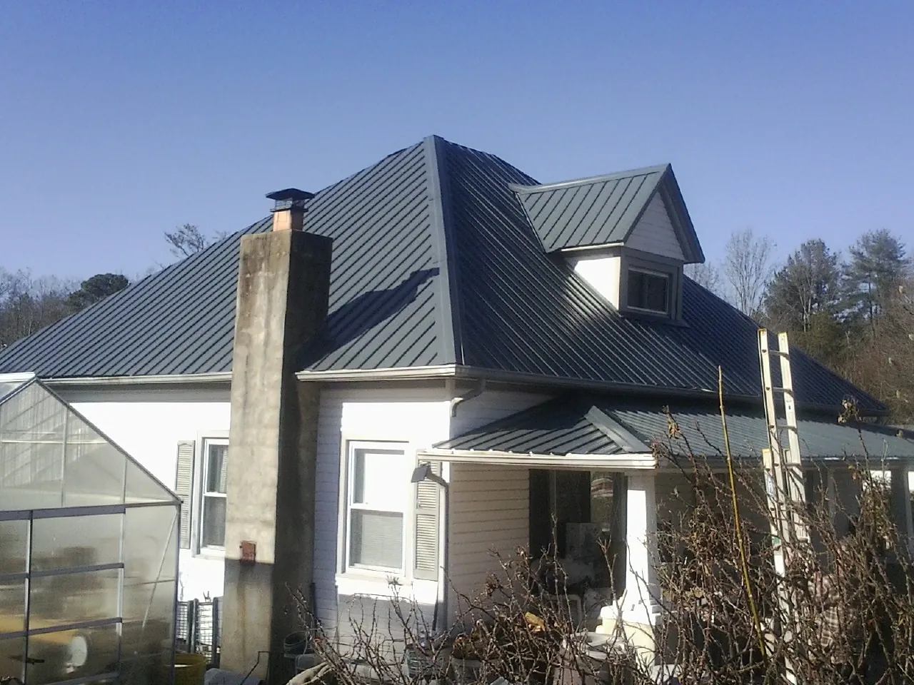 Dark blue standing seam metal roof on a white farmhouse with dormer — Slate & Tile Roof Repair by Roofing Brothers in Castalia