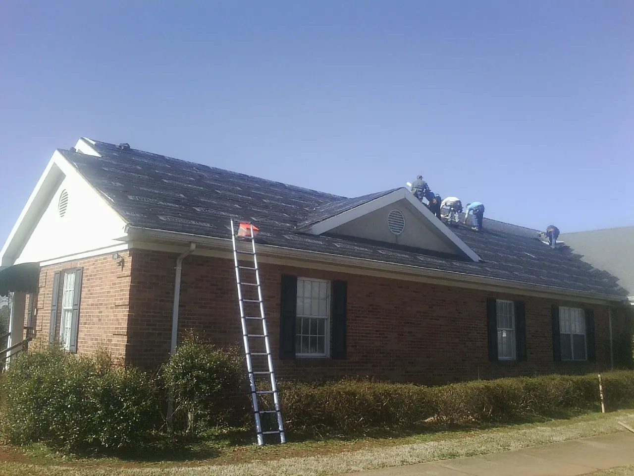 Crew tearing shingles off a brick ranch roof with a ladder set — Emergency Roof Repair work by our crew in Castalia