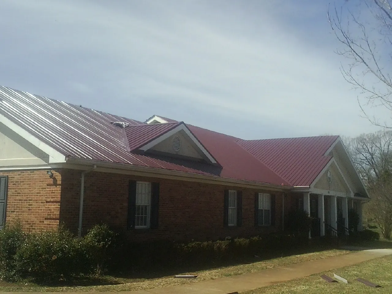 Red metal roof with gabled entries on a long brick building, from a Hail Damage Roof Repair job in Castalia