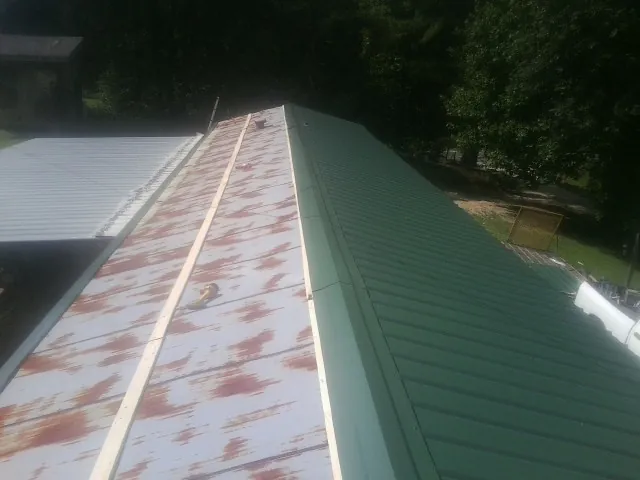 Old rusted panels beside newly installed green metal roofing — Wind Damage Roof Repair by Roofing Brothers in Castalia