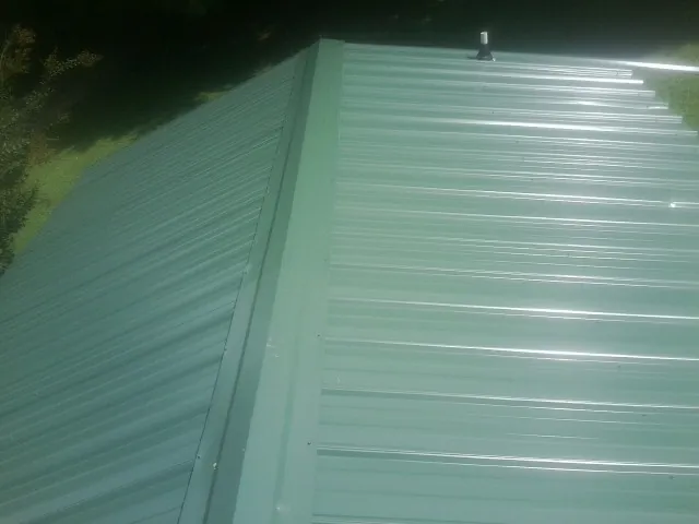 New green metal panels meeting at the ridge of a roof — Flat Roof Repair work by our crew in Castalia