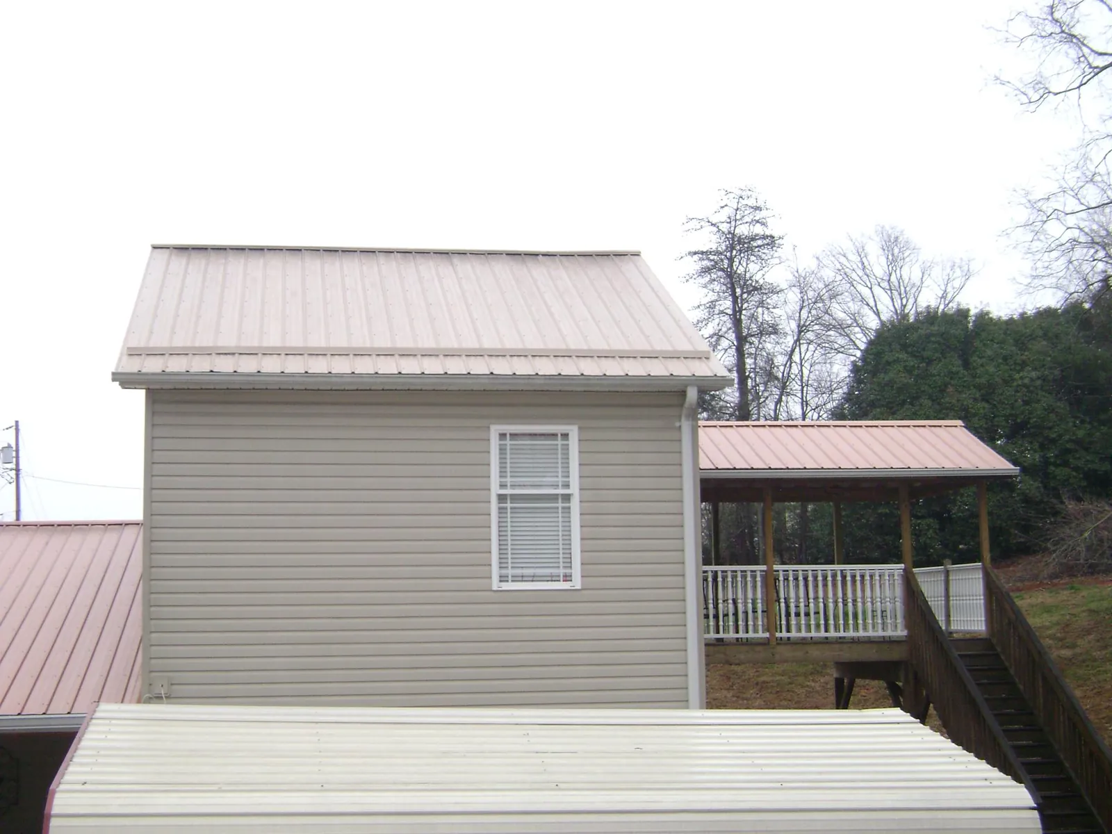 Tan metal roofs on a two story addition and attached porch, from a Roof Replacement job in Castalia